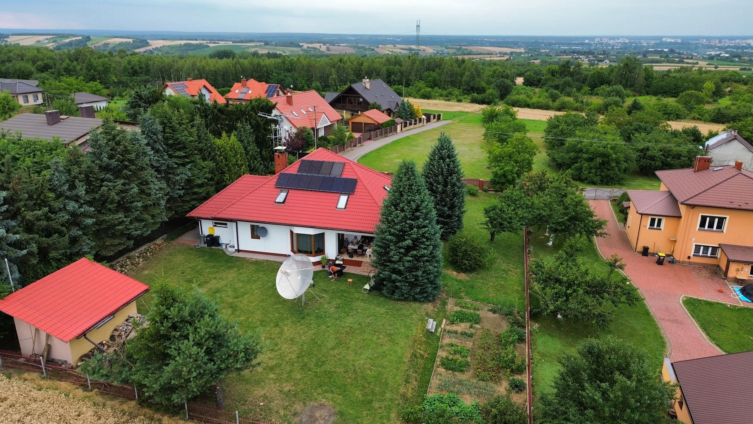 Ogród i dom z anteną paraboliczną na tle zabudowy i otaczających pól.