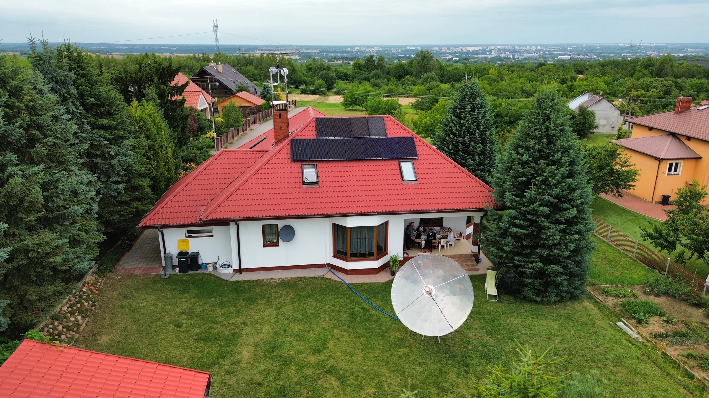 Ujęcie z drona przedstawiające dom, ogród i dużą antenę paraboliczną przed budynkiem.