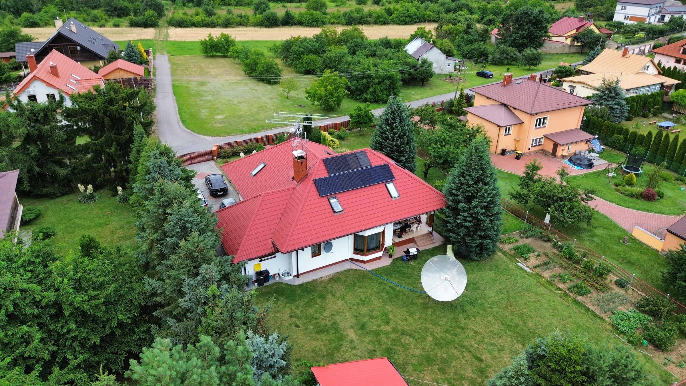 Szerokie ujęcie posesji z czerwonym dachem, ogrodem i białą czaszą anteny.