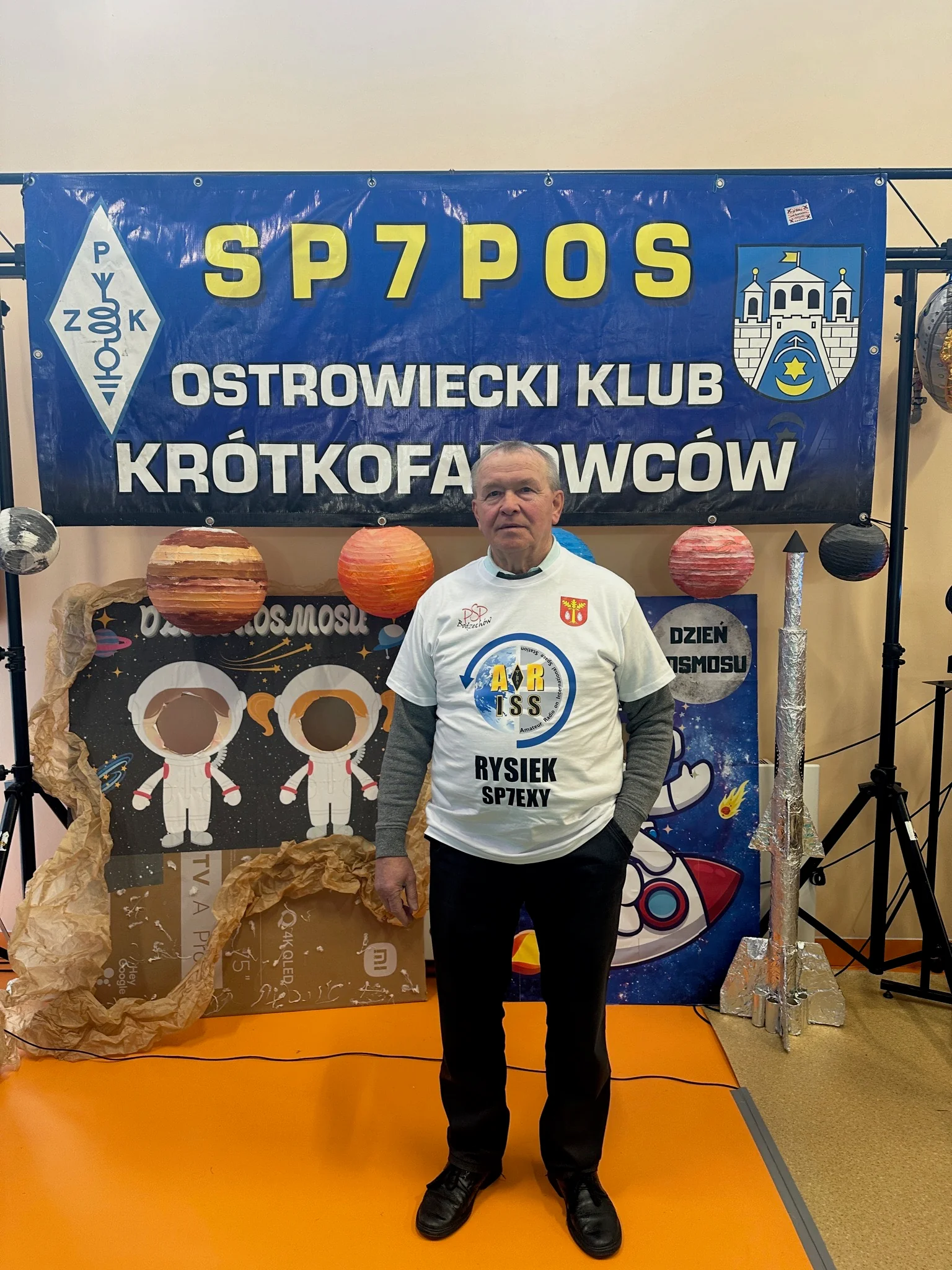 Ryszard Więcaszek w koszulce ARISS ze znakiem SP7EXY, przed banerem klubu SP7POS.