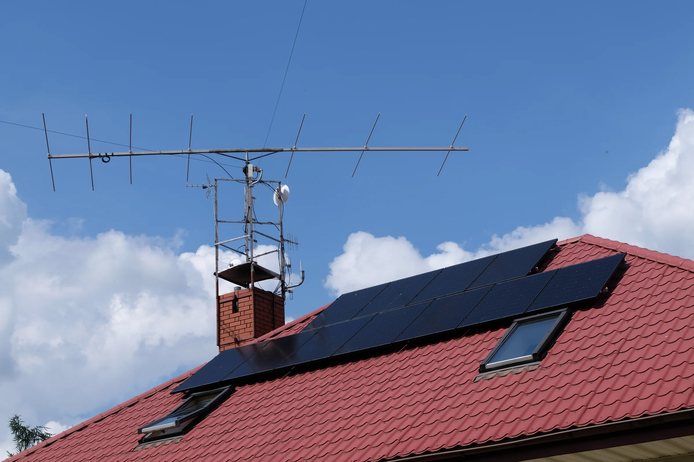 Antena kierunkowa na kominie ponad czerwonym dachem i panelami słonecznymi.