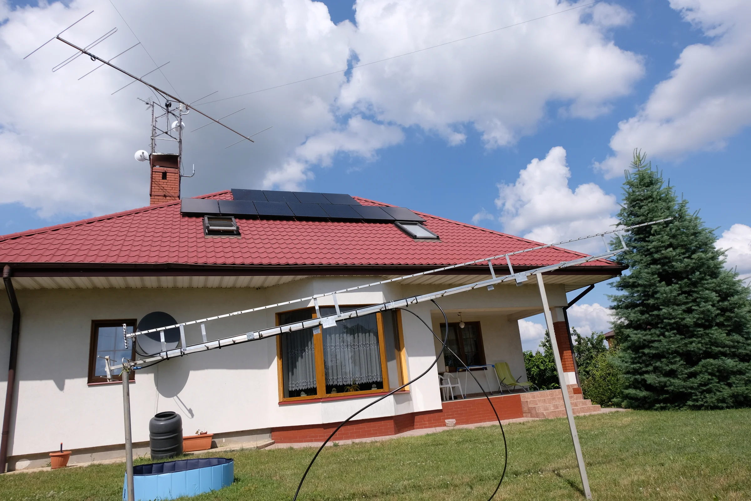 Dom z anteną na kominie oraz długą anteną ustawioną w ogrodzie.