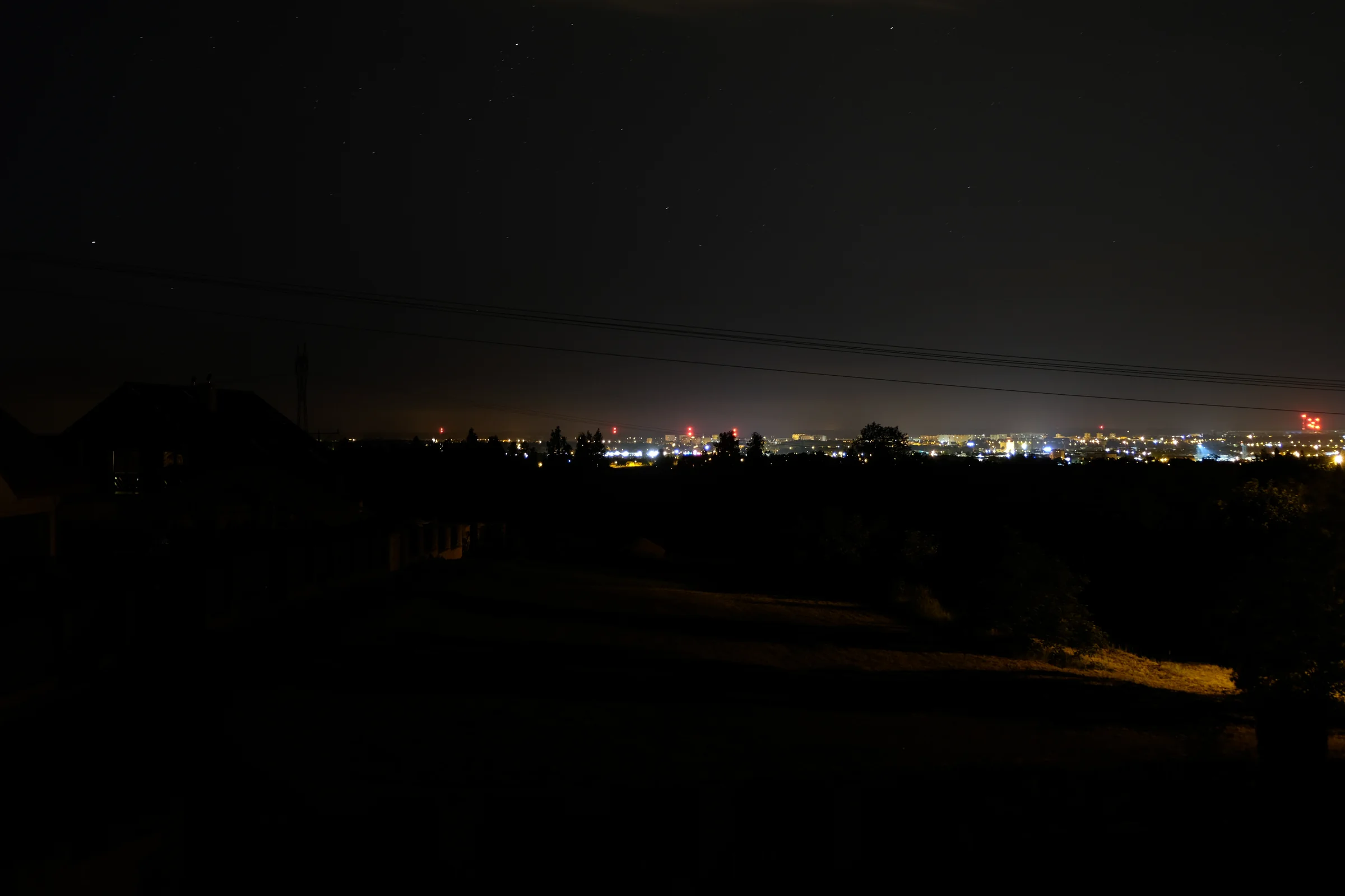 Światła miasta na horyzoncie widoczne nocą ponad ciemnym krajobrazem.